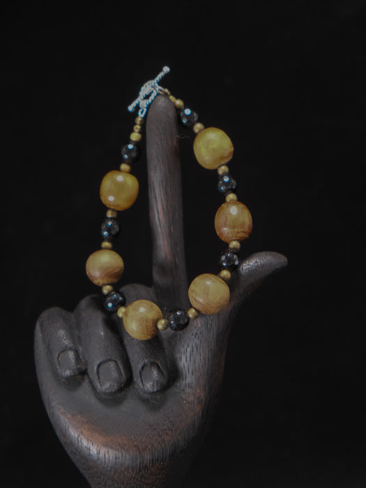 Bracelet with yellow and black beads on a wooden hand sculpture against a dark background