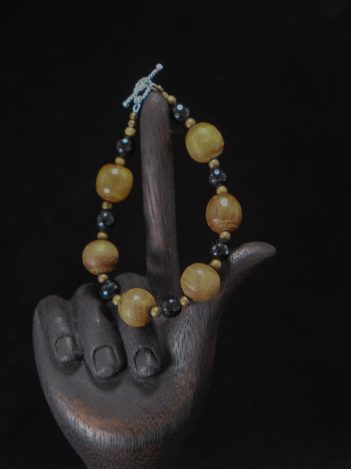 Bracelet with yellow and black beads on a wooden hand sculpture against a dark background