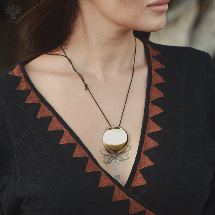 Close-up of a person wearing a necklace with a gold pendant on a black garment.
