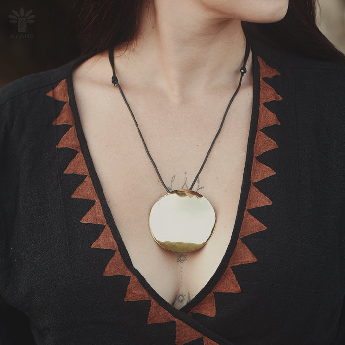 Person wearing a necklace with a large pendant, set against a dark background.