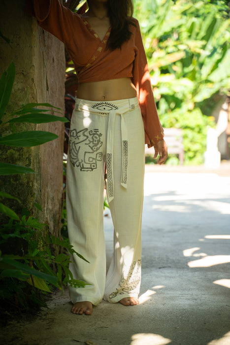 Person wearing a brown top and white pants with patterns, standing in a natural setting.