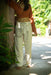Person wearing a brown top and white pants with patterns, standing in a natural setting.