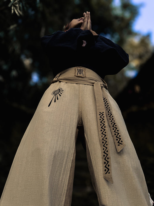 Person wearing beige pants with black patterns and designs, standing against a blurred natural background.