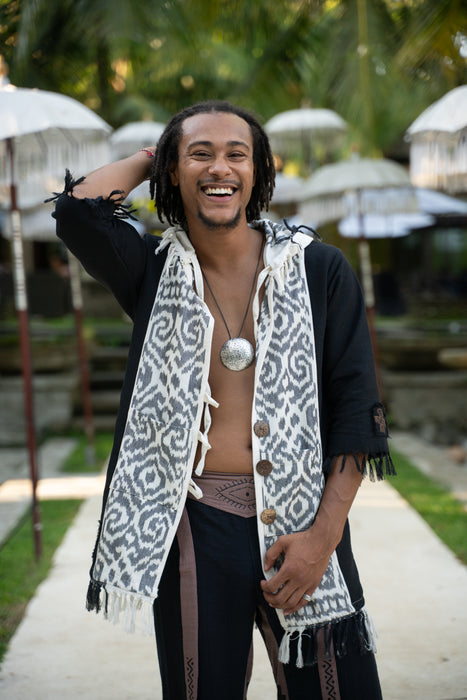 Man with dreadlocks wearing a patterned scarf in an outdoor setting with umbrellas.