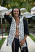Man with dreadlocks wearing a patterned scarf in an outdoor setting with umbrellas.