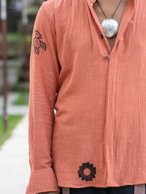Person wearing a peach-colored shirt with black patterns, standing outdoors.