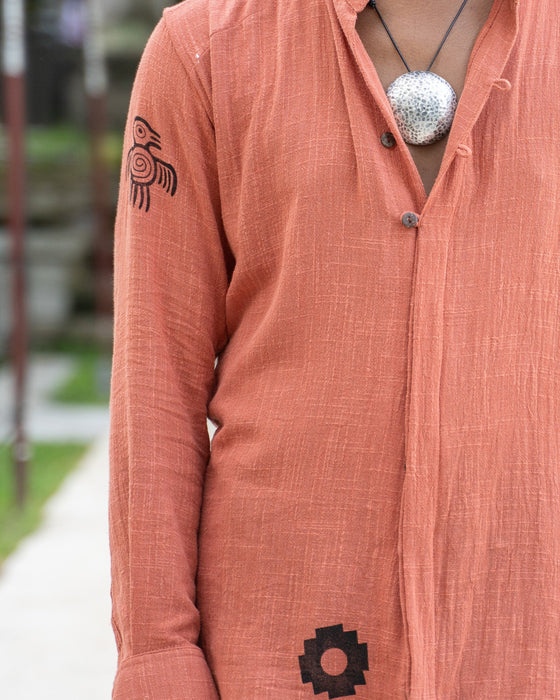Person wearing a peach-colored shirt with black patterns, standing outdoors.