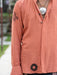 Person wearing a peach-colored shirt with black patterns, standing outdoors.