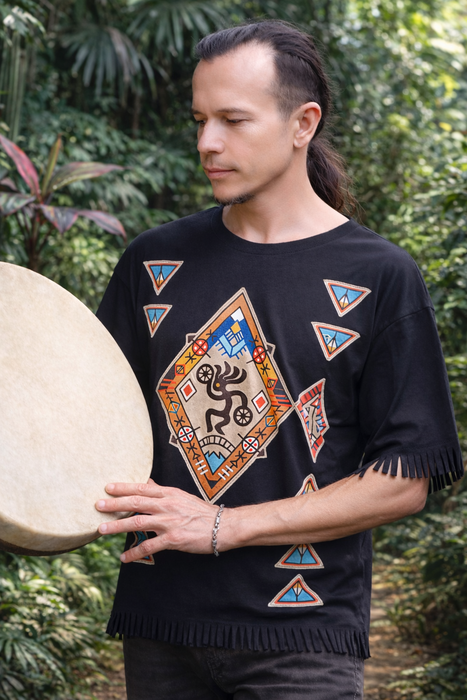 Person wearing a black sweater with colorful geometric patterns, holding a drum outdoors.