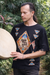 Person wearing a black sweater with colorful geometric patterns, holding a drum outdoors.