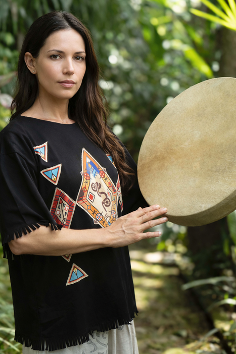 Woman holding a large round drum outdoors with greenery in the background