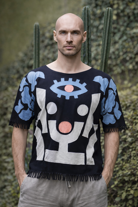 Man wearing a black sweater with abstract designs in front of cacti