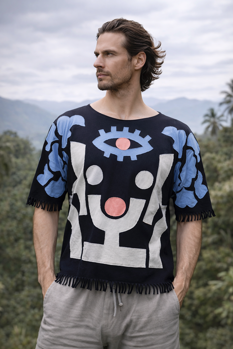 Man wearing a black sweater with abstract designs in blue, white, and pink against a natural background.