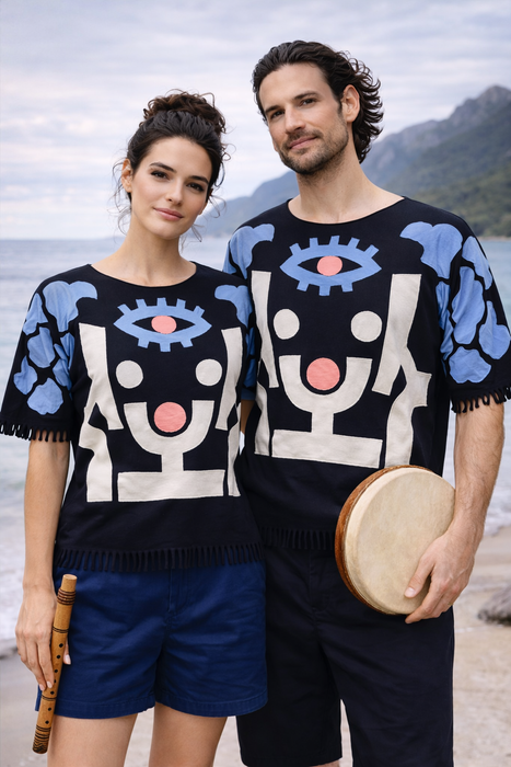 Two people wearing matching black sweaters with abstract patterns standing by a body of water.