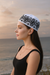 Woman wearing a black and white patterned headscarf against a sunset beach backdrop