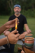Person lighting a small ceramic cup with a flame, with another person sitting in the background.