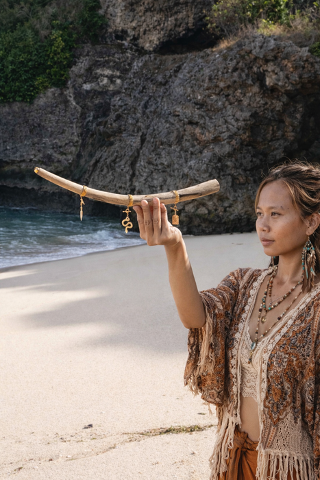 Woman holding a long, curved object on a beach with rocky cliffs in the background