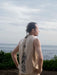 Person wearing a sleeveless shirt with a design, standing by the ocean.