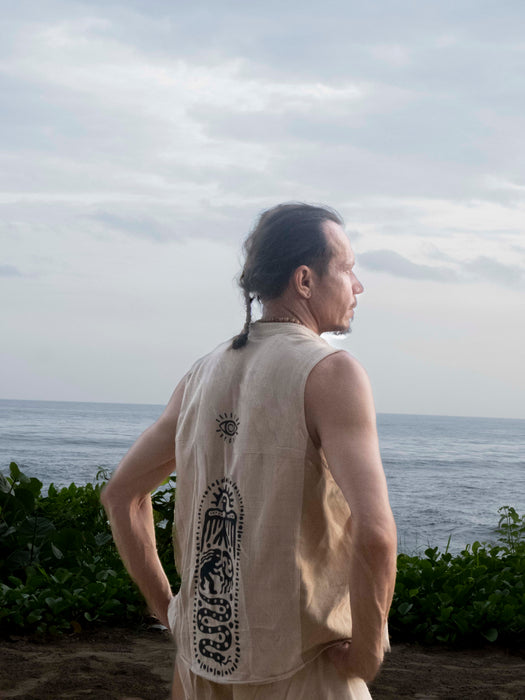 Person wearing a sleeveless shirt with a design, standing by the ocean.