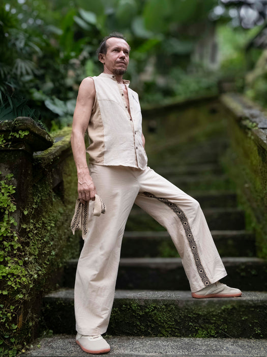 Man in beige vest and pants standing on a mossy staircase with greenery in the background