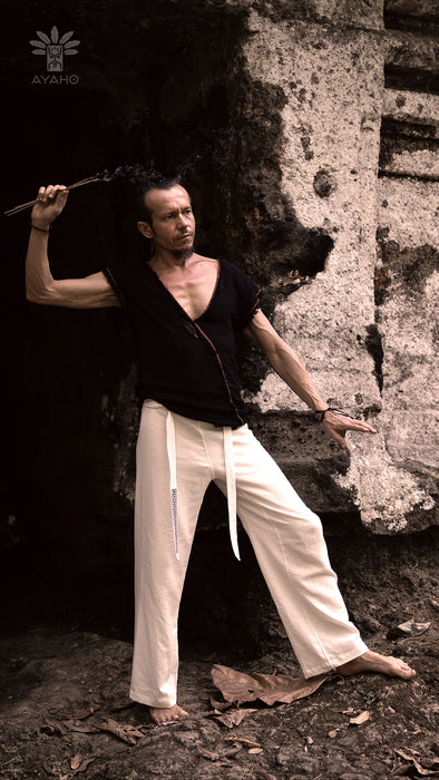 Man in black shirt and white pants holding a staff against a stone wall.
