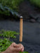 Hand holding a cylindrical incense stick with a blurred natural background