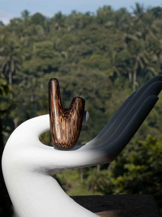 White sculpture with a wooden element against a forest background