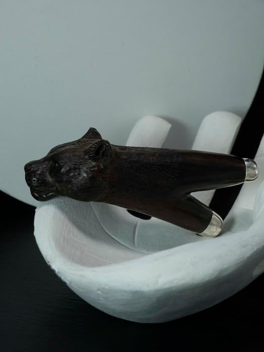 Dark brown animal-shaped object on a white stand against a light gray background