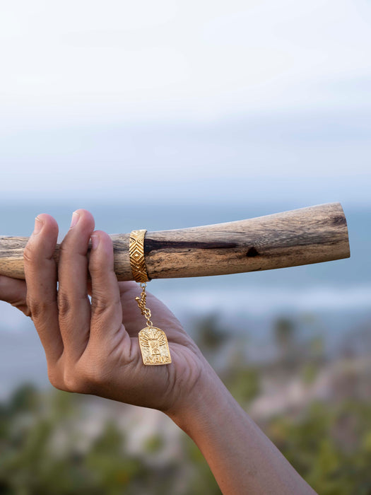 Hand holding a gold bracelet on a wooden stick with a blurred natural background