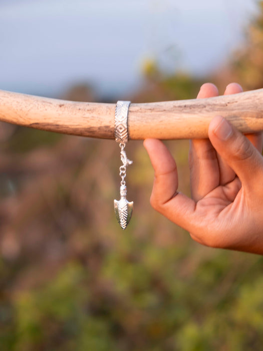 Silver bracelet with an arrow pendant on a wooden stick against a natural background
