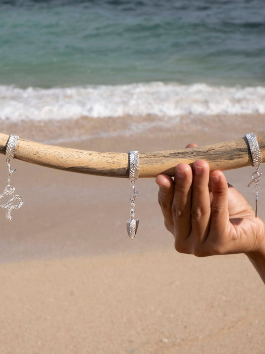 Hand holding a driftwood with silver earrings against a beach background