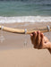 Hand holding a driftwood with silver earrings against a beach background