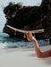Hand holding a curved piece of driftwood with charms against a rocky beach backdrop