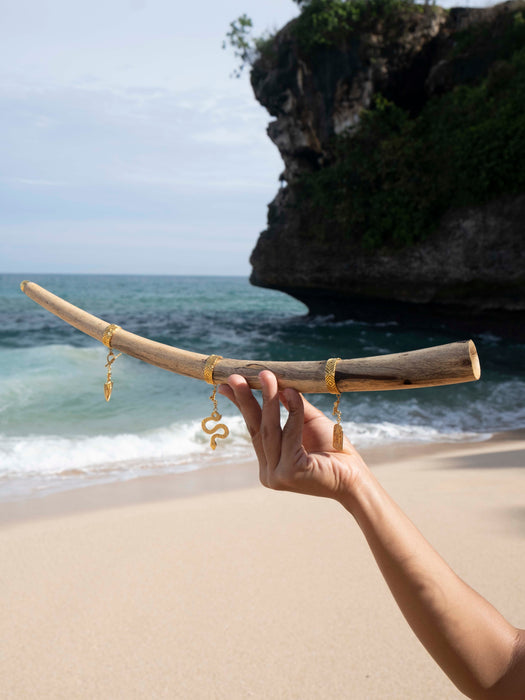 Hand holding a piece of driftwood with gold jewelry against a beach backdrop