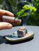 Hand holding a Yawanawa Shungite bottle over an incense burner with smoke rising.