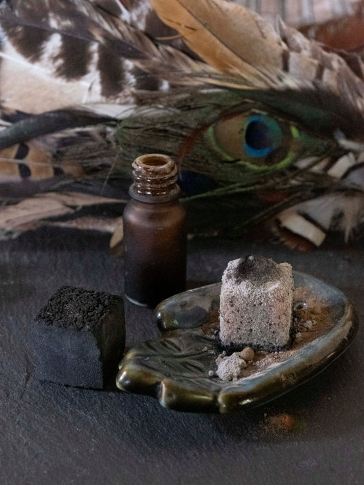 Small brown bottle with peacock feather and stone on dark surface