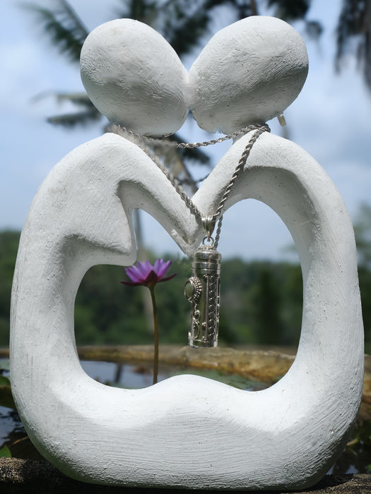 White stone sculpture of two figures embracing with a necklace, set against a natural background.