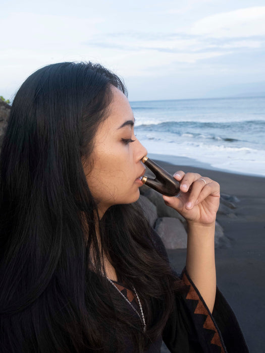 Woman drinking from a bottle on a beach with ocean waves in the background