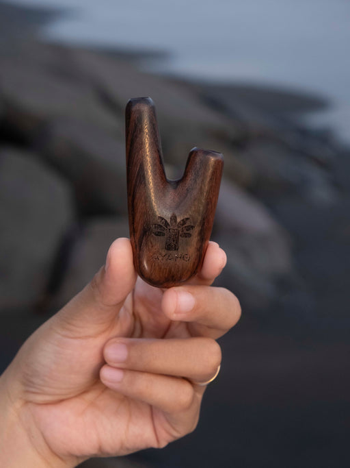 Hand holding a wooden archery bow nock against a blurred natural background