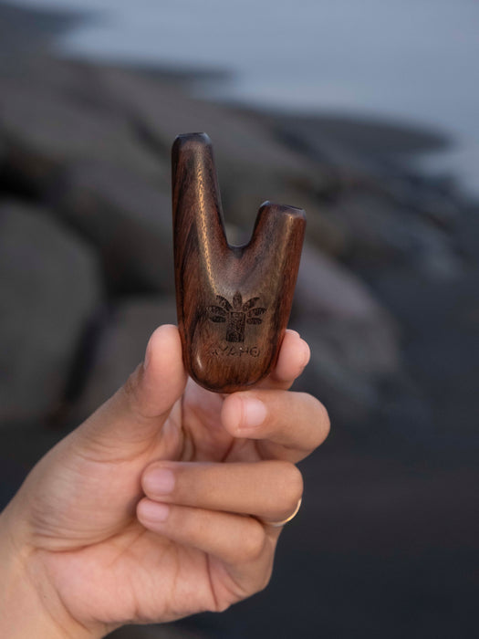 Hand holding a wooden archery bow nock against a blurred natural background