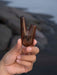 Hand holding a wooden archery bow nock against a blurred natural background