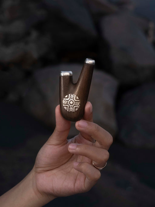 Hand holding a wooden tool with intricate carvings against a blurred natural background