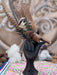 Black hand sculpture holding a small brown bird against a decorative background