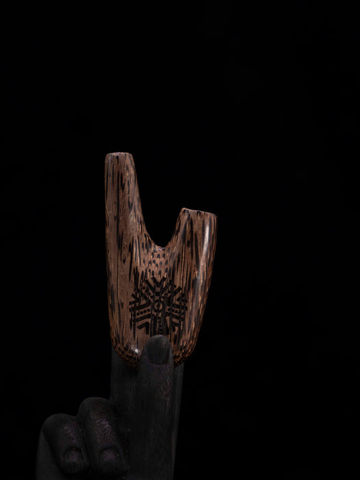Wooden tool with intricate patterns held by a hand against a black background