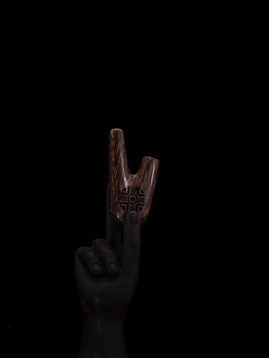 Wooden tool with engraved design held by a hand against a black background