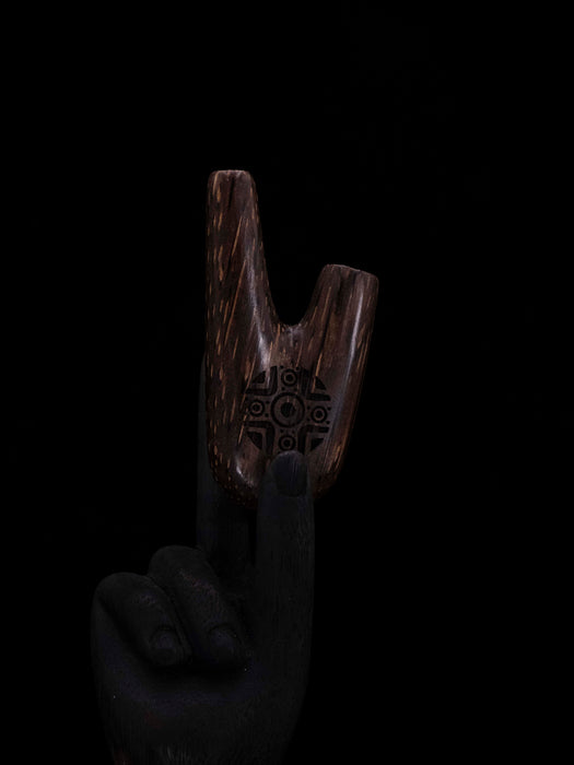Wooden tool with engraved design held by a gloved hand against a black background