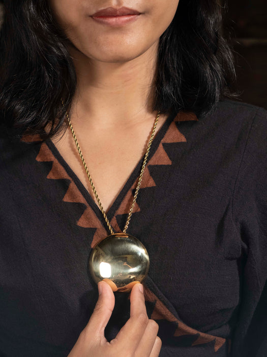Person wearing a dark top with a V-neckline, holding a gold necklace with a large pendant.