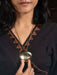 Person wearing a dark top with a V-neckline, holding a gold necklace with a large pendant.