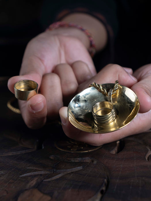 Close-up of hands holding a small brass tray with coins and a ring.