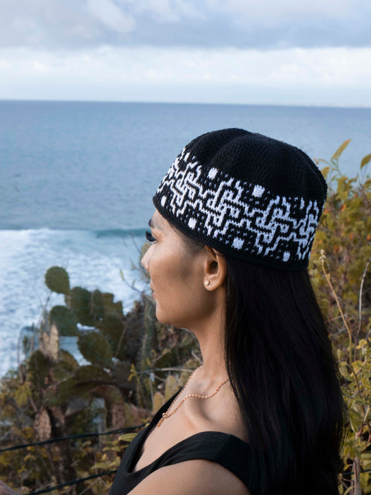 Woman wearing a black and white patterned beanie with ocean and cacti in the background